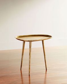 a small table with wooden legs and a gold plate on it's side, sitting on a hard wood floor