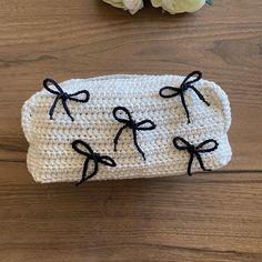 a crocheted case with black bows on it sitting on a table next to flowers