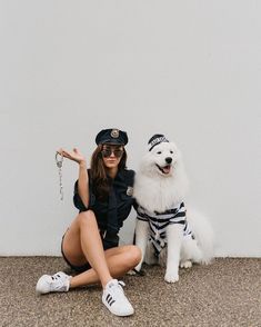 a woman sitting on the ground next to a white dog wearing a police uniform and holding a chain