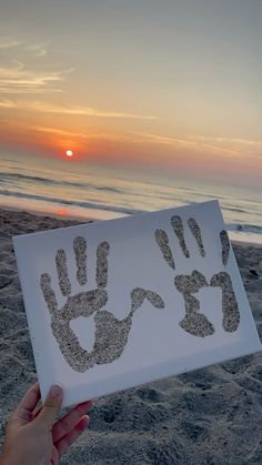 someone is holding up a sign with hand prints on it at the beach as the sun sets