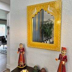 a mirror and two figurines on a table in front of a yellow framed mirror