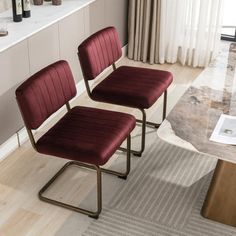 two red chairs sitting on top of a rug in front of a table with wine bottles