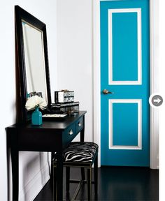 a blue door in a white room with a black table and mirror on the floor