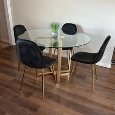 a glass table with black chairs and a potted plant on the top, in front of a white wall