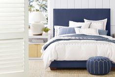 a bed with white and blue sheets, pillows and blankets on top of it in a bedroom