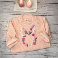 a pink sweater with flowers on it next to two candles and a plate that says i love you