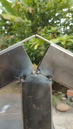 a metal object sitting on top of a table next to some trees and bushes in the background