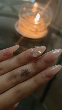 a woman's hand with a small flower tattoo on her left thumb and a lit candle in the background