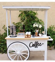 an outdoor coffee cart is set up with flowers and greenery on the sidelines