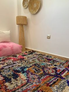 a room with a colorful rug and two pillows on the floor next to a lamp