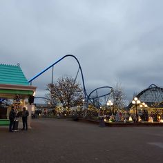 two people standing in front of a roller coaster at the amusement park during christmas time