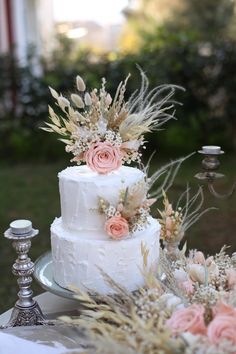 a white wedding cake with pink flowers and greenery on the top is surrounded by silver candlesticks