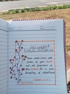 an open notebook with arabic writing on the page and flowers in it, sitting next to a sidewalk