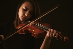 a woman is playing the violin on a dark background