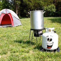 an outdoor stove with a pot on it next to a tent in the grass and a campfire