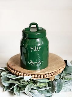 a green canister sitting on top of a wooden tray next to eucalyptus leaves and greenery