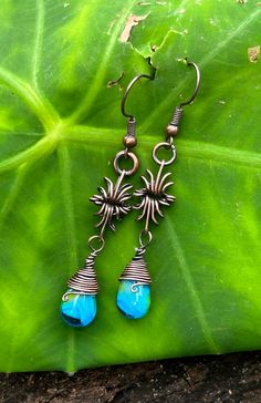 the earrings are made from metal wire and blue glass beads, on top of a green leaf