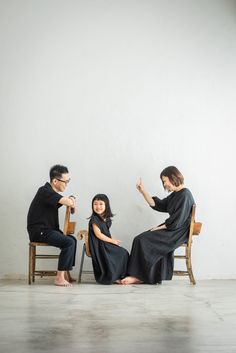 three people sitting on chairs in front of a white wall and one person pointing at something