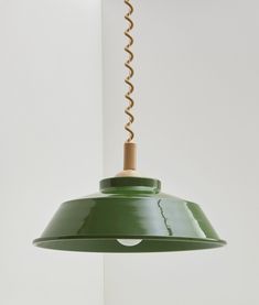 a green light hanging from a ceiling with a white wall in the background and a wooden stick sticking out of it