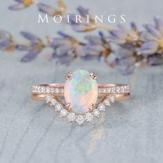 a white opal and diamond ring sitting on top of a table next to lavender flowers