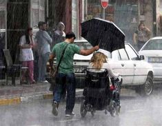 a man pushing a woman in a stroller with an umbrella on a city street