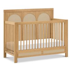 a wooden crib with white sheets on the bottom and beige fabric around the sides