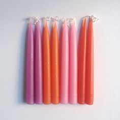 four orange and pink candles sitting next to each other on a white surface with string