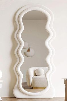 a large white mirror sitting on top of a wooden floor next to a chair and table