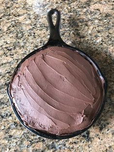 a chocolate cake in a cast iron skillet on a granite counter top with a black handle