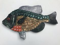 a metal fish with green and orange scales on it's back legs, sitting on a white surface