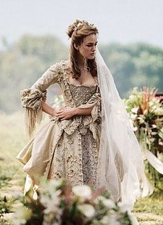 a woman dressed in an old fashion wedding gown and veil walking down the aisle with her hand on her hip