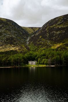 a house on the shore of a lake surrounded by mountains