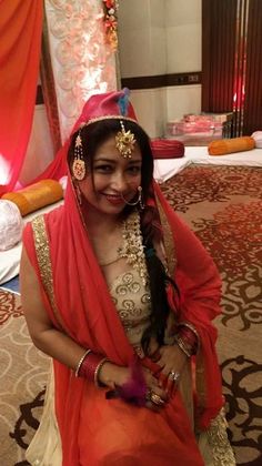 a woman sitting on the floor in an orange and white sari with gold jewelry