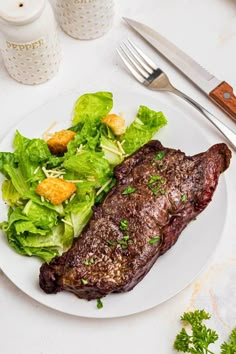 a plate with steak, lettuce and croutons on it next to a knife and fork