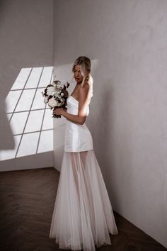 a woman in a white dress is holding a bouquet and posing for the camera with her shadow on the wall behind her