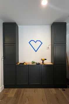 a kitchen with black cabinets and blue heart painted on the wall above it, along with wood flooring