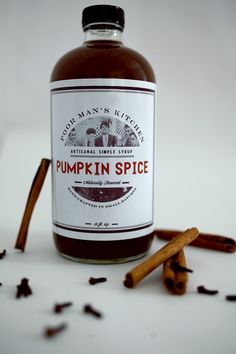 a bottle of pumpkin spice next to cinnamon sticks and cloves on a white surface