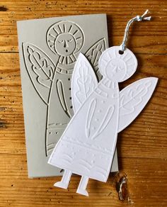 a white paper angel ornament sitting on top of a wooden table next to a card