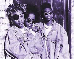 three young women standing next to each other in front of a brick wall wearing sunglasses