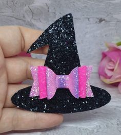 a hand holding a small black and pink glittered hat with a bow on it