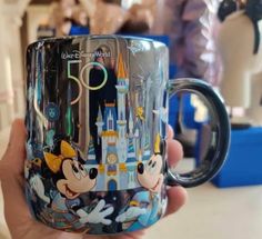 someone holding up a coffee mug with mickey mouse and other disney characters in front of them