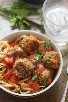 a white bowl filled with spaghetti and meatballs next to a glass of ice water