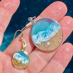 a hand holding a pair of earrings with an ocean scene on it