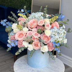 a blue vase filled with pink and white flowers on top of a marble table next to a mirror