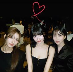 three young women sitting next to each other in front of a red heart on the wall