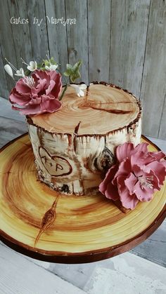 a cake decorated with wood and flowers on a wooden plate next to a fence board