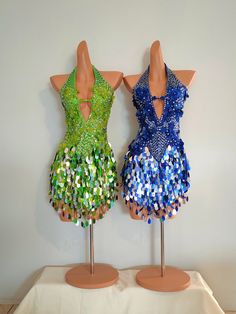 two mannequins dressed in colorful sequins on wooden stands with white backdrop