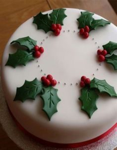 a cake decorated with holly leaves and red berries on a wooden tableclothed surface