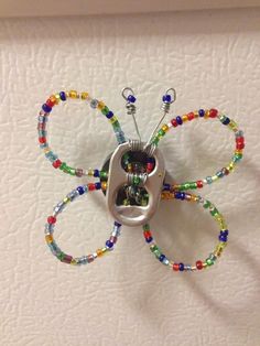 a metal butterfly with multicolored beads hanging from it's back end on a white wall