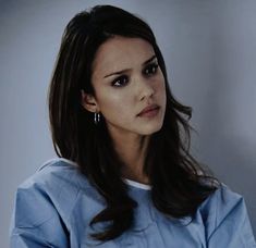 a woman with long dark hair wearing a blue shirt and earrings looking at the camera